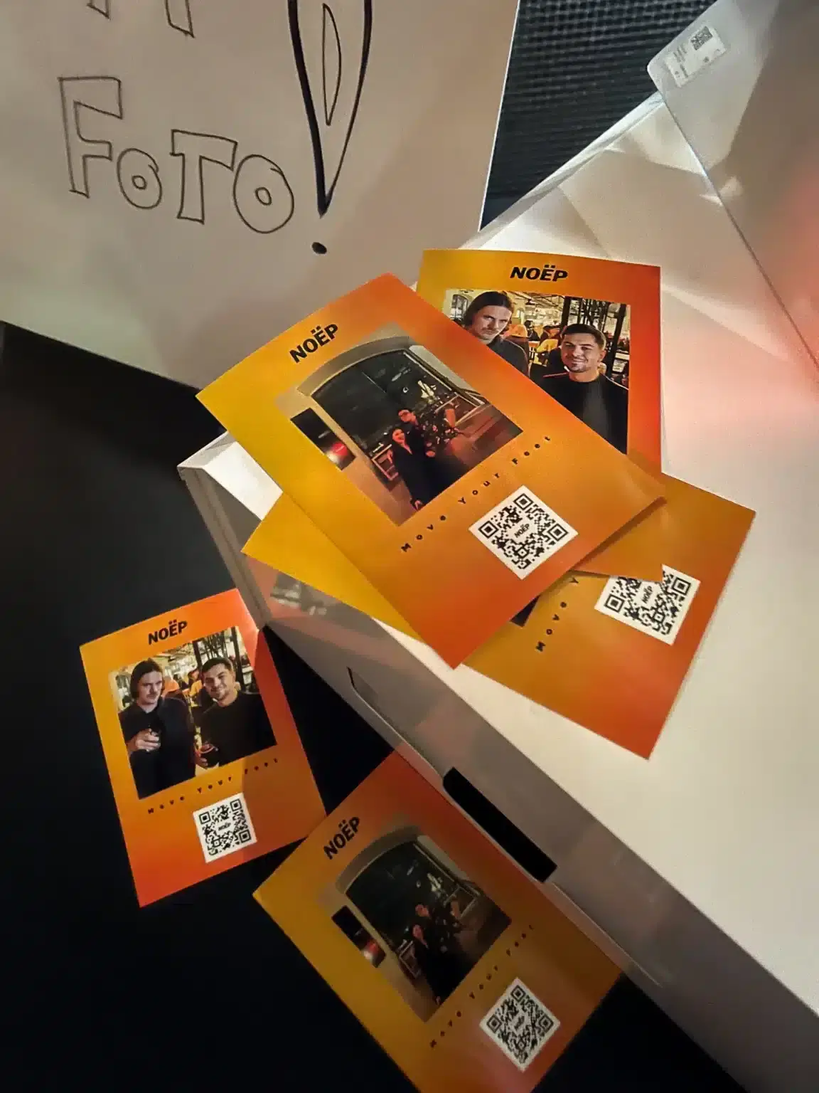 Vairākas oranžas Insta Print izdrukas ar QR kodiem uz galda