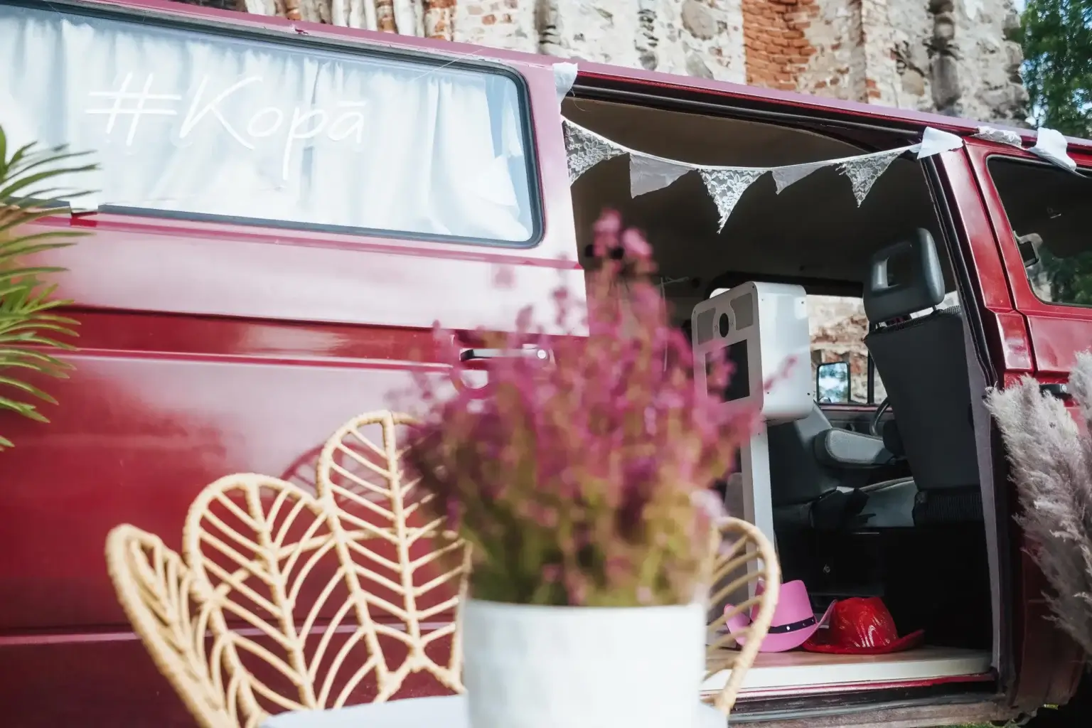 Sarkans VW T3 busiņš ar atvērtām sānu durvīm un ziedu dekoru pie ieejas
