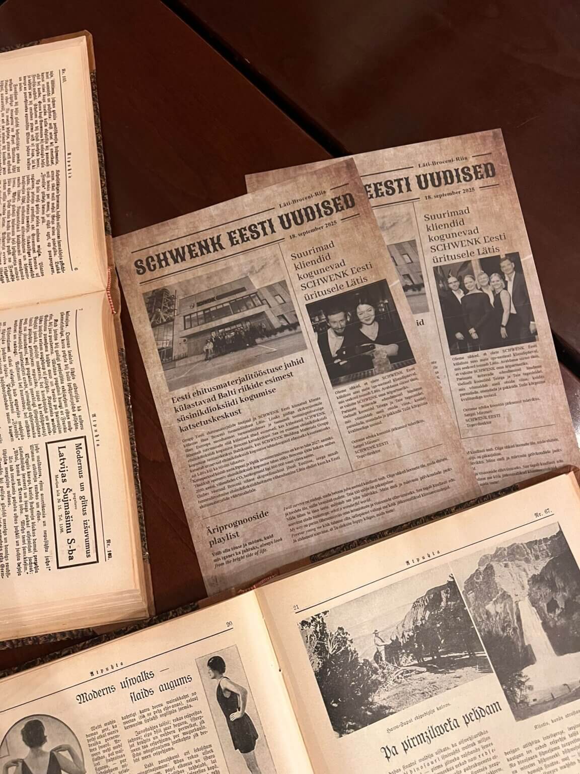 Trīs foto avīzes ar uzņēmuma bildēm uz galda blakus vecai grāmatai