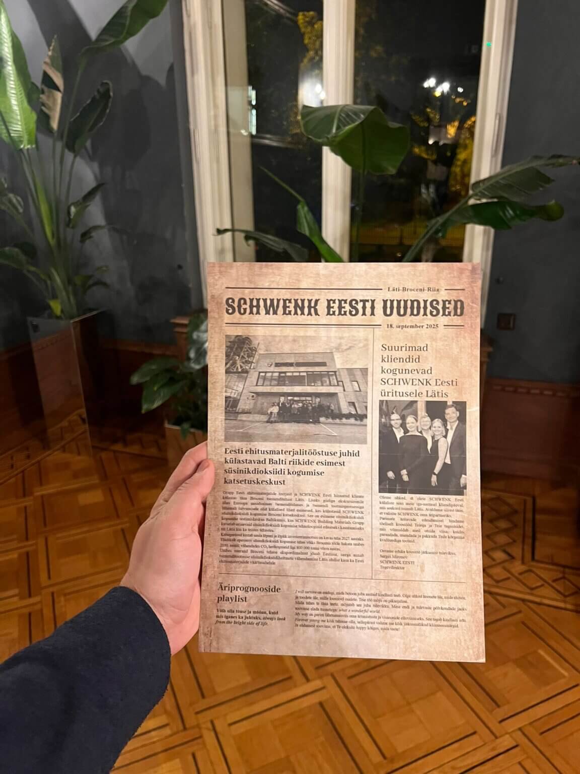 Roka tur foto avīzi ar uzņēmuma nosaukumu un komandas bildi pie loga; foto avīze A4 pasākumā
