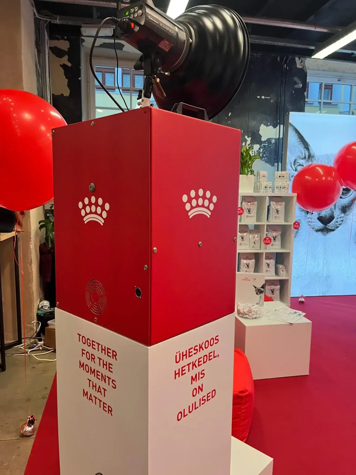 Sarkana foto kaste ar Royal Canin zīmola aplīmējumu un sarkaniem baloniem pasākuma telpā
